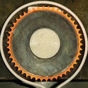 Ein Kettenrad wird durch Induktionserwärmung gehärtet. Der Prozess zeigt die Wärmebehandlung, bei der ein Teil des Kettenrads durch elektromagnetische Induktion erhitzt wird